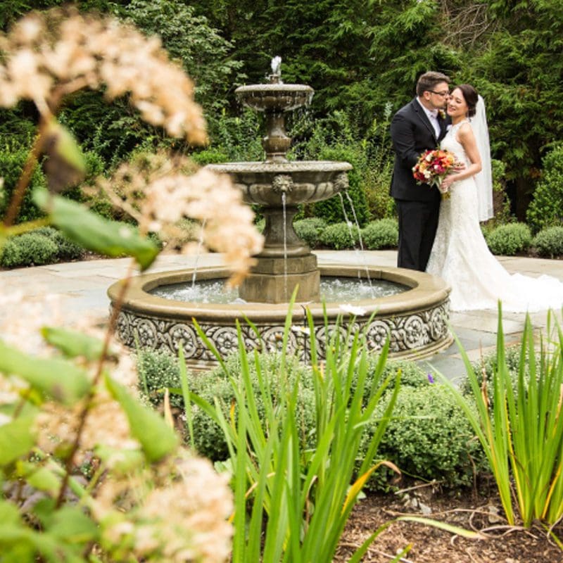 bride and groom embracing behind a water fountain