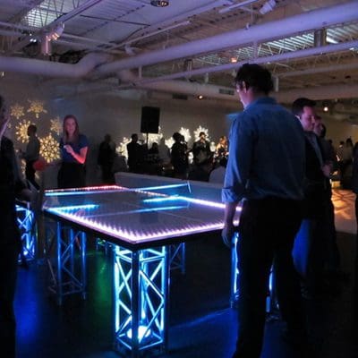 guests playing ping pong at a lit up table