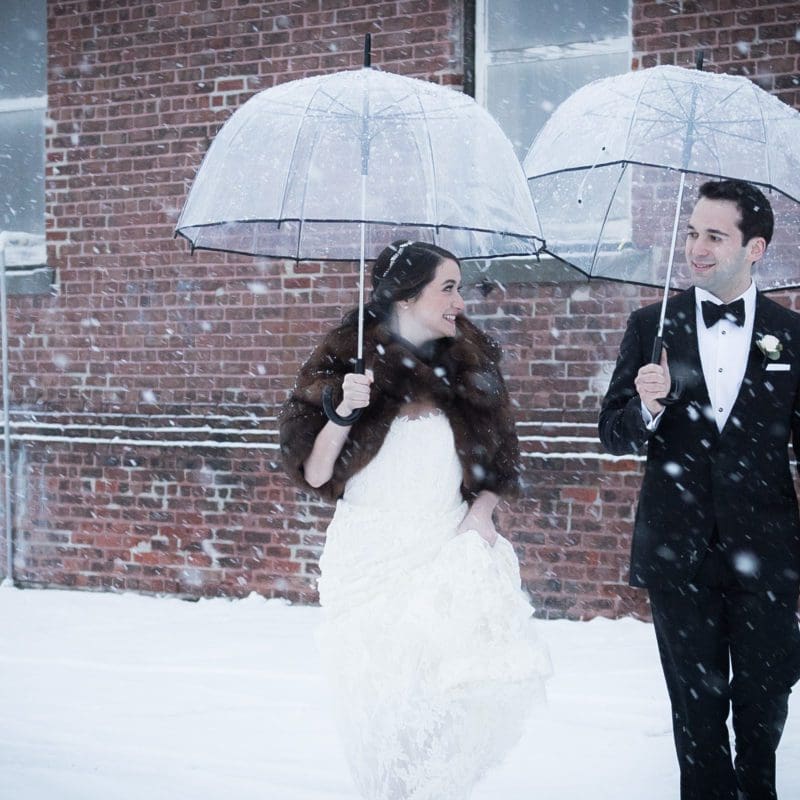 bride and groom outside in the snow holding umbrellas
