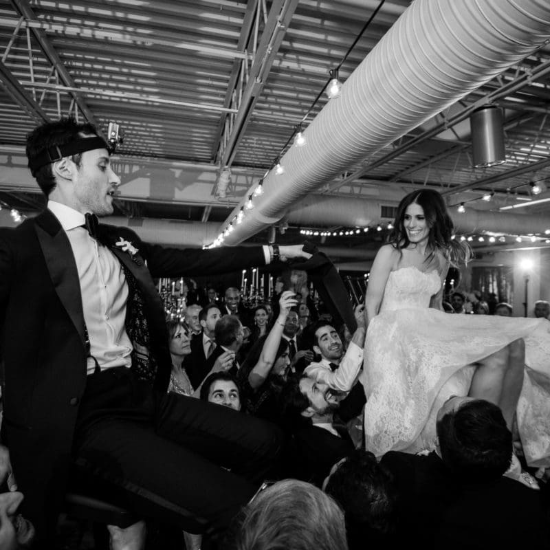 bride and groom being lifted up in chairs by guests