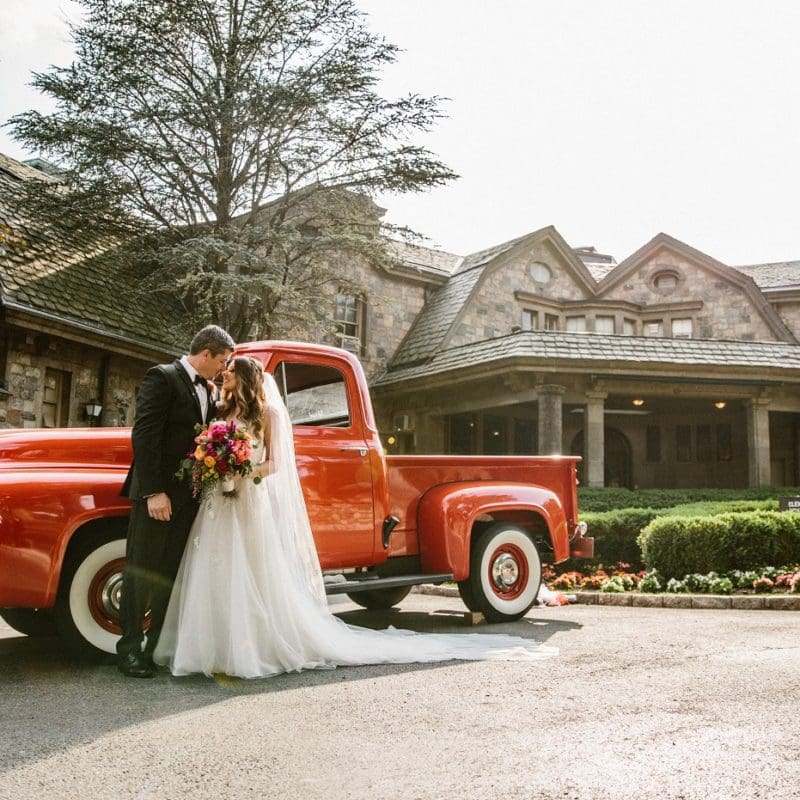 bride and groom embracing in front of antique car