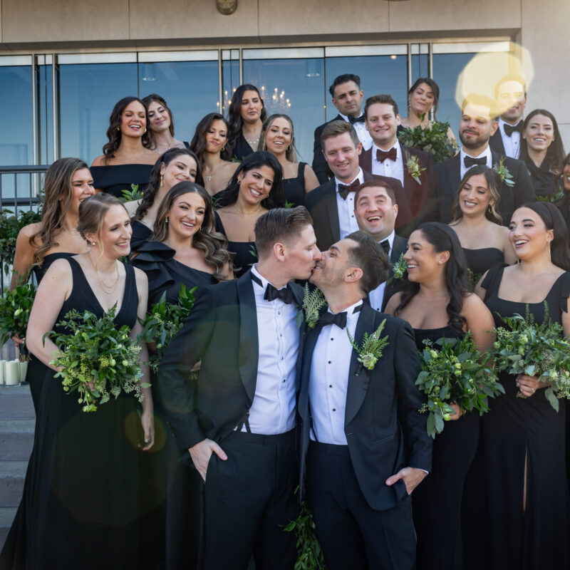 Two grooms and wedding party pose outside of event space.