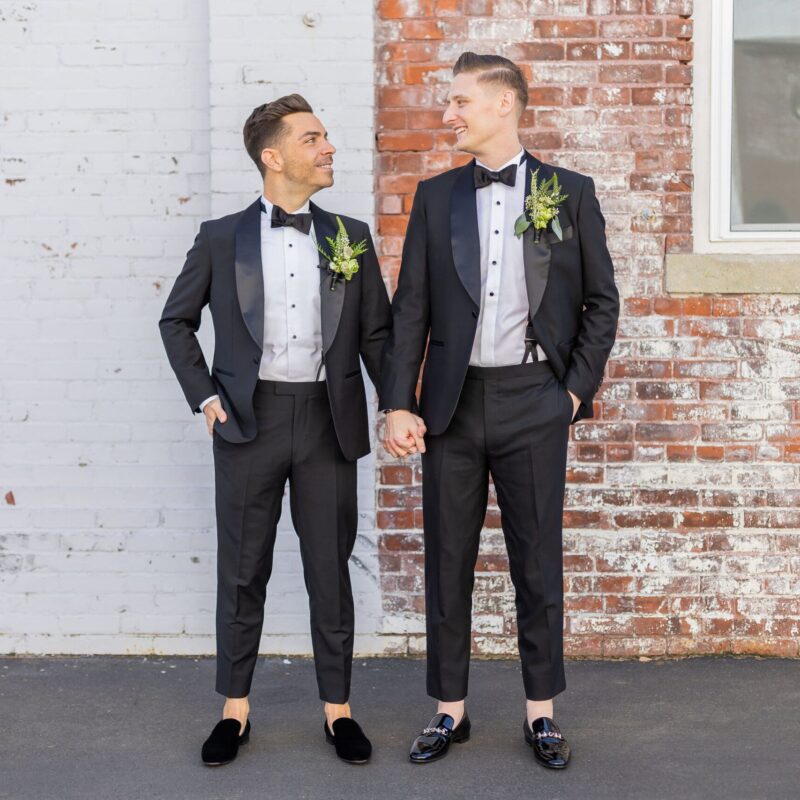 Grooms pose in outdoor area.